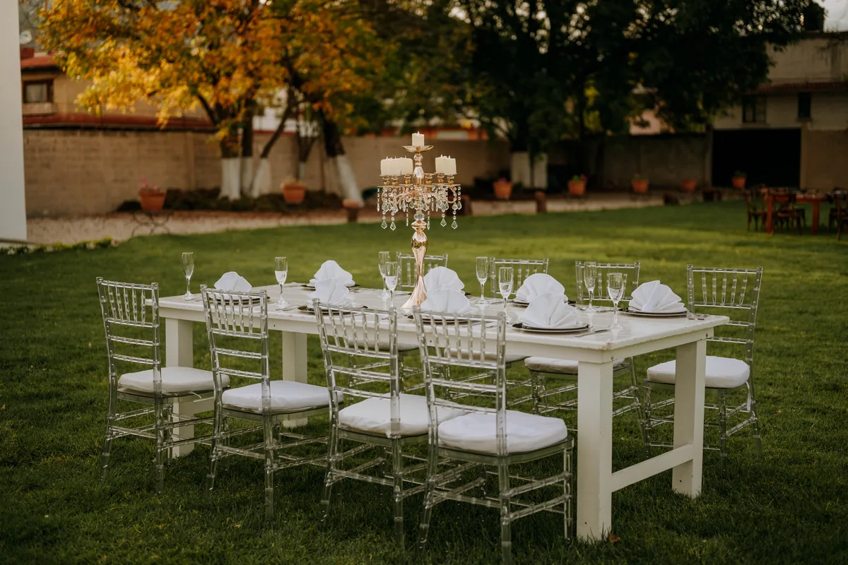 Mesa blanca con sillas acrílicas y candelabro en el jardín al anochecer